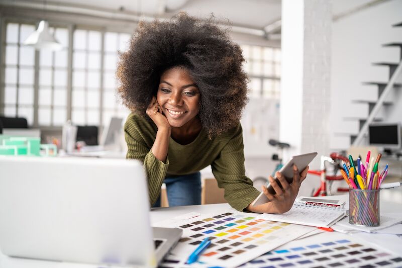 Jeune femme souriante travaillant dans un bureau coloré, illustrant le quotidien varié du métier de conseiller en image - Première Impression