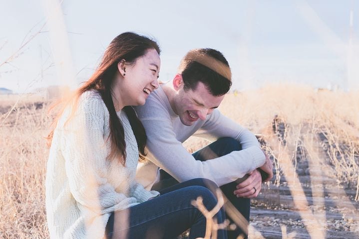 Couple souriant en plein air lors d’un premier rendez-vous, partageant un moment complice et détendu.